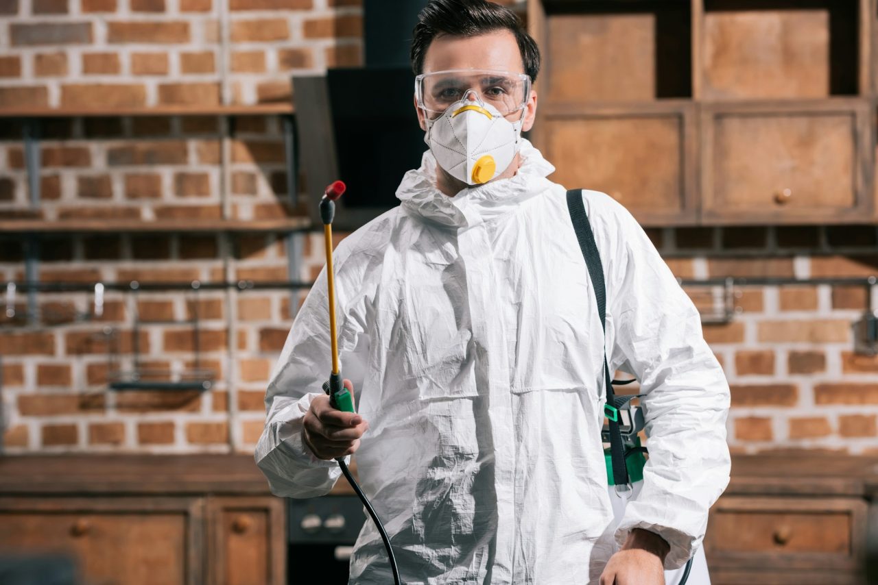 Pest control worker standing in kitchen with sprayer and looking at camera